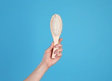 Photo of Woman holding wooden hair brush against blue background, closeup