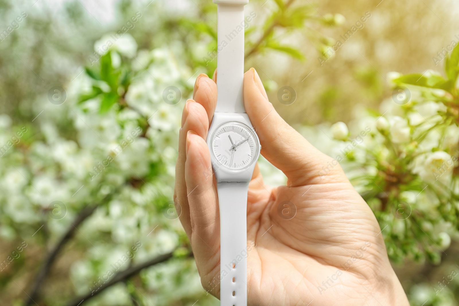 Photo of Woman holding beautiful wristwatch on blurred background, focus on hand. Time change concept