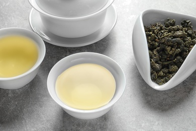 Cups of Tie Guan Yin oolong and chahe with tea leaves on grey table