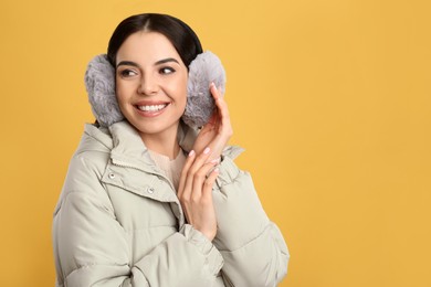 Photo of Beautiful young woman wearing earmuffs on yellow background. Space for text