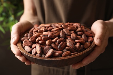 Photo of Woman holding wooden bowl of cocoa beans, closeup view