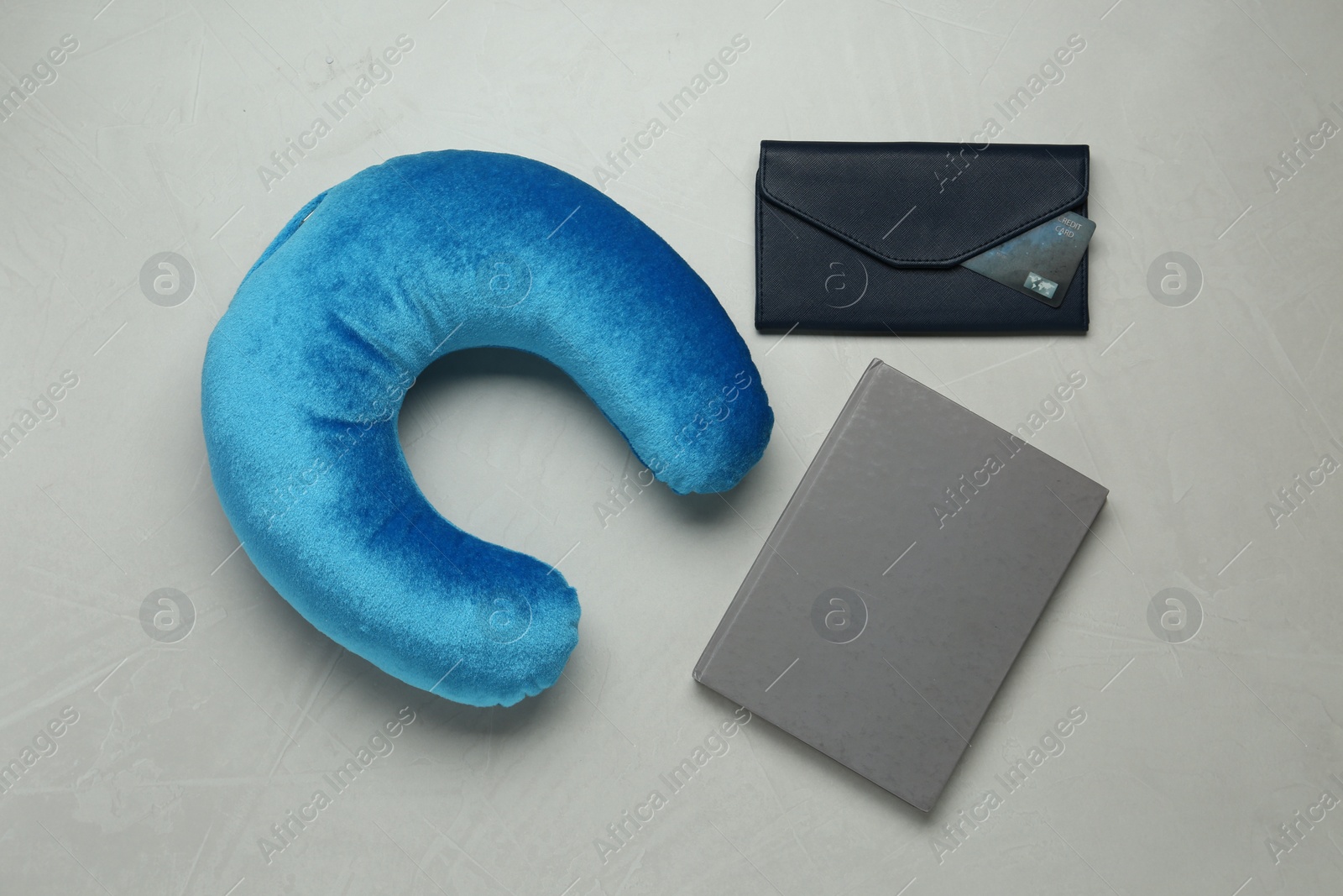 Photo of Light blue travel pillow, notebook and wallet with credit card on gray background, flat lay