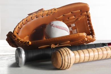 Baseball glove, bats and ball on white wooden table, closeup