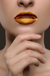 Young woman with beautiful gold lips on grey background, closeup