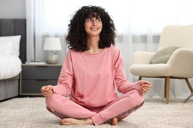 Beautiful young woman in stylish pyjama meditating on floor at home