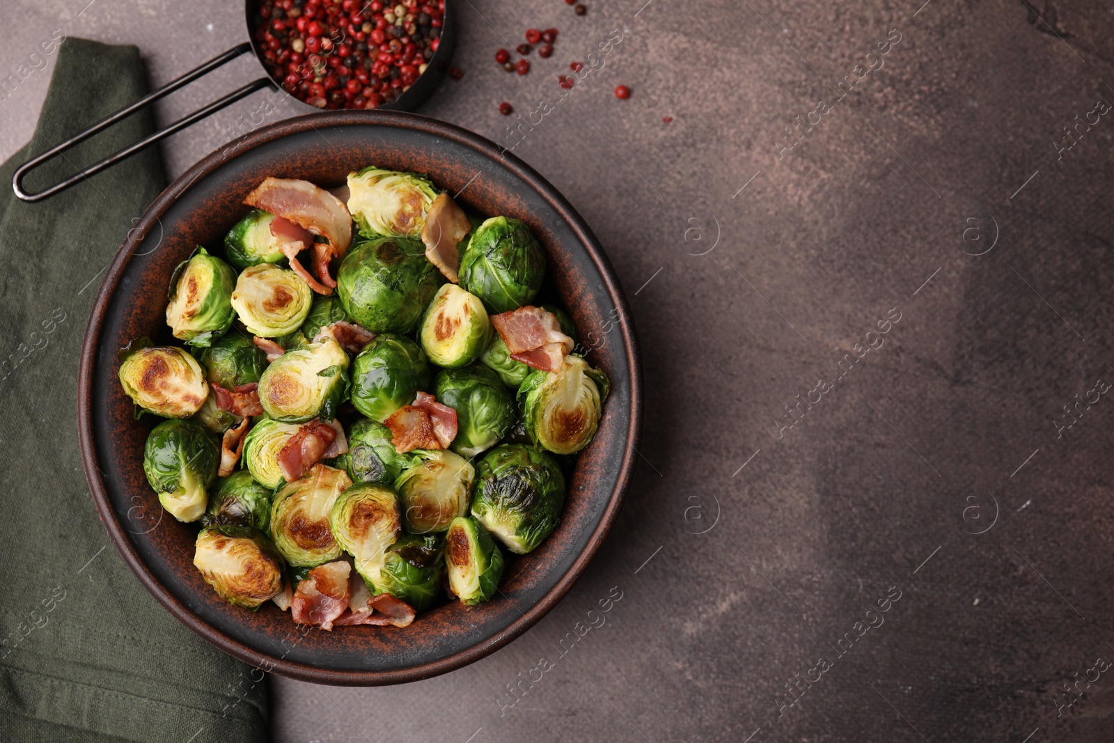 Photo of Delicious roasted Brussels sprouts, bacon and peppercorns on brown table, top view. Space for text