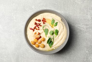 Photo of Tasty hummus with garnish in bowl on grey table, top view