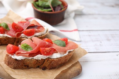Photo of Tasty bruschettas with prosciutto, tomatoes and cheese on white wooden table, closeup