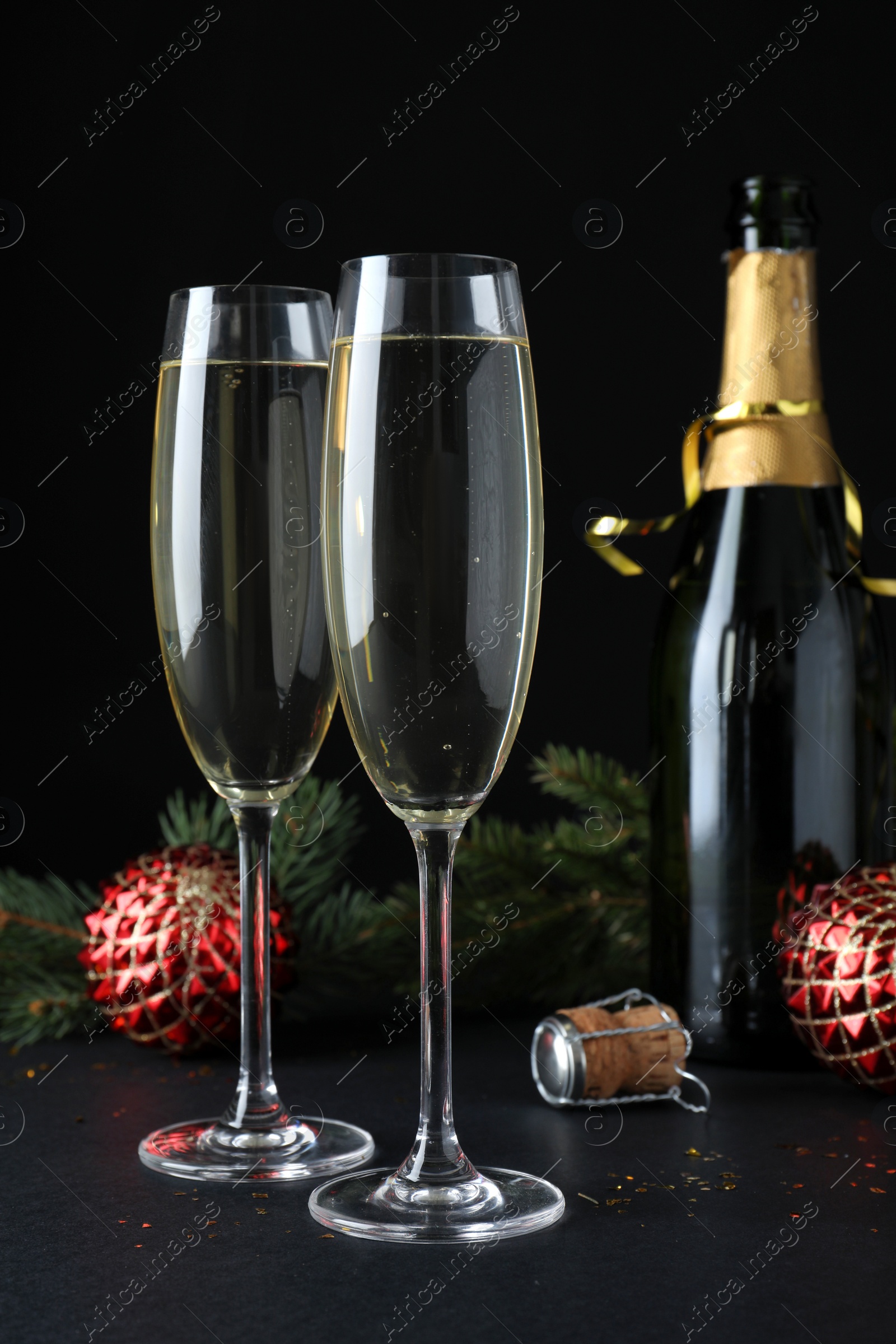 Photo of Happy New Year! Bottle of sparkling wine, glasses and festive decor on table against black background