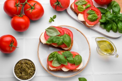 Delicious Caprese sandwiches with mozzarella, tomatoes, basil and other ingredients on white table, flat lay