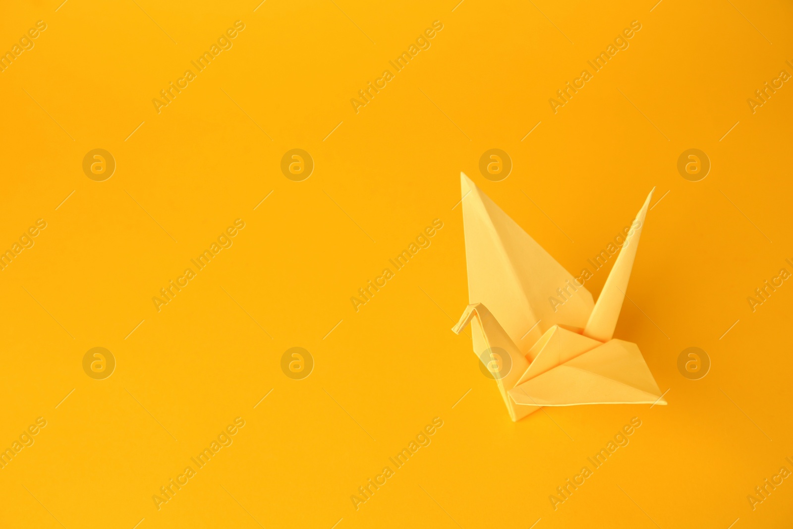 Photo of Origami art. Beautiful light yellow paper crane on orange background, space for text