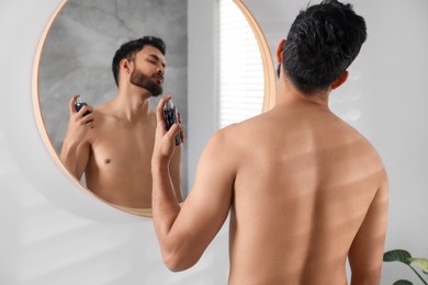 Man spraying luxury perfume near mirror indoors