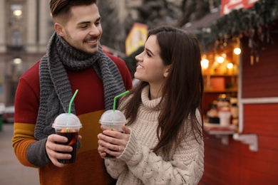Photo of Young couple with cups of mulled wine at winter fair