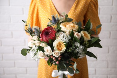 Woman with bouquet of beautiful roses near white brick wall, closeup