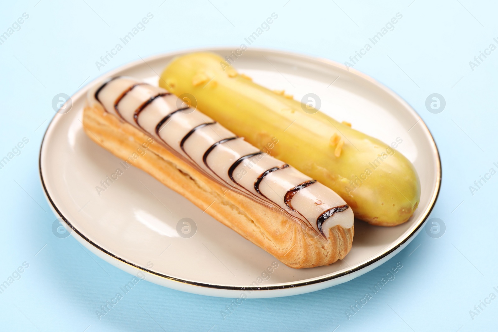 Photo of Delicious eclairs covered with glaze on light blue background