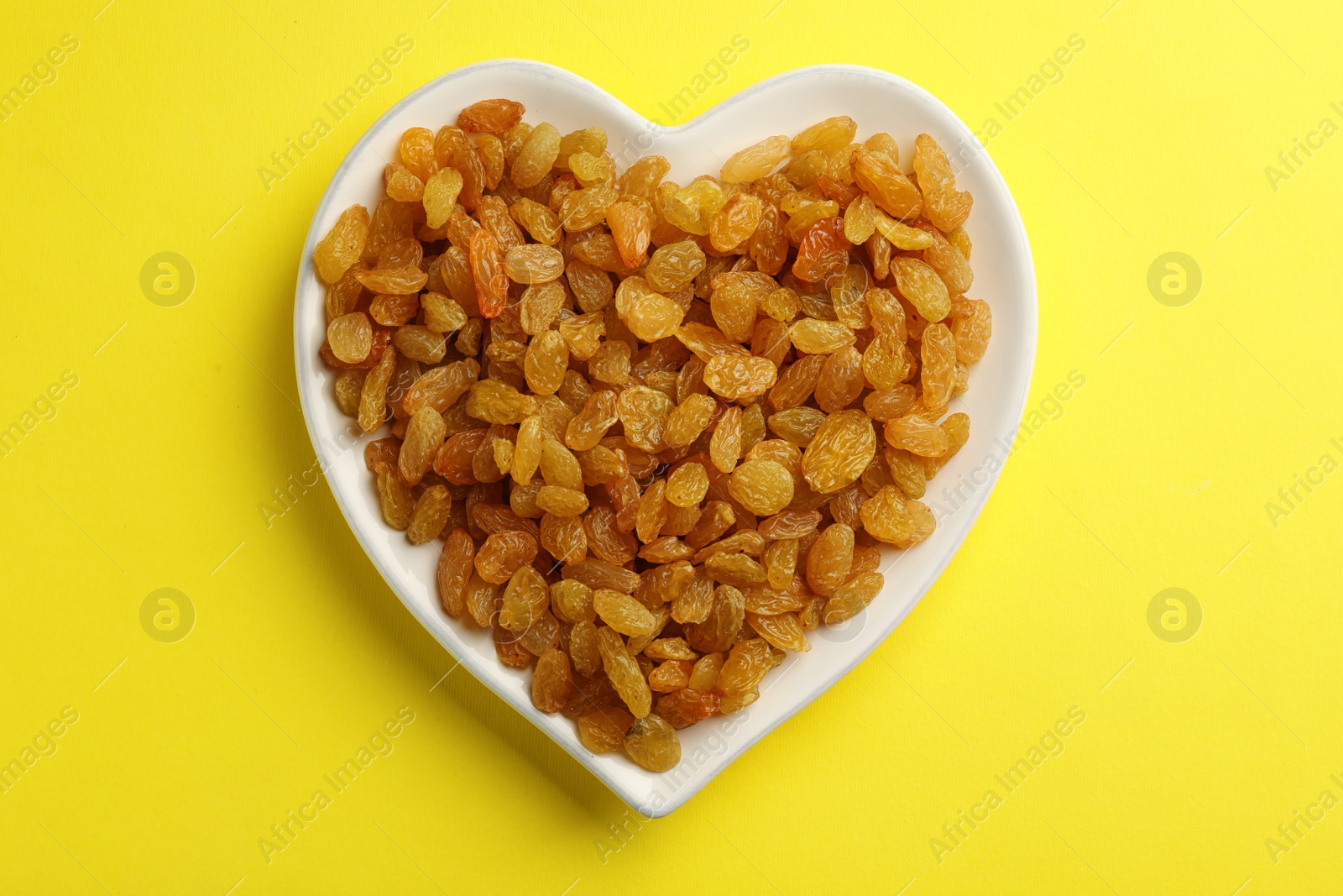 Photo of Heart shaped plate with raisins on color background, top view. Dried fruit as healthy snack