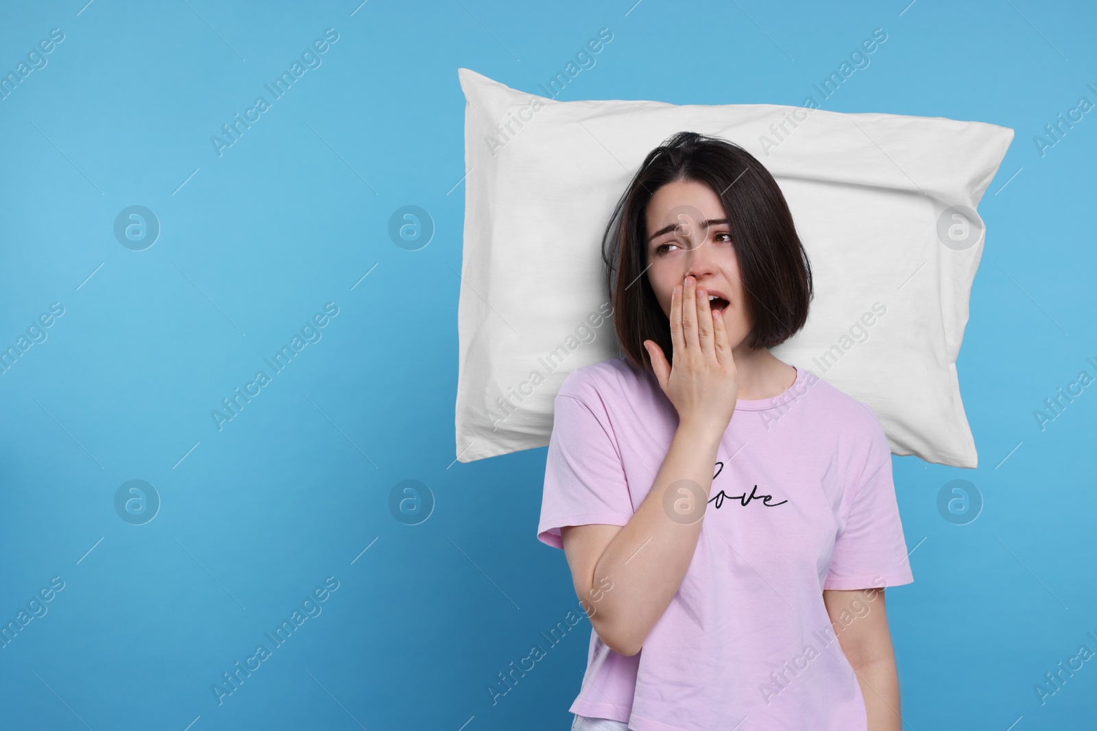 Photo of Sleepy young woman with pillow yawning on light blue background, space for text. Insomnia problem