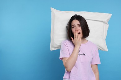 Sleepy young woman with pillow yawning on light blue background, space for text. Insomnia problem