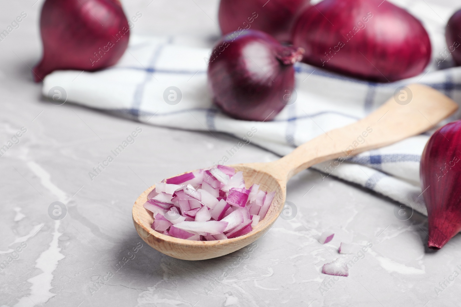 Photo of Spoon with cut and whole red onions and napkin on grey marble table