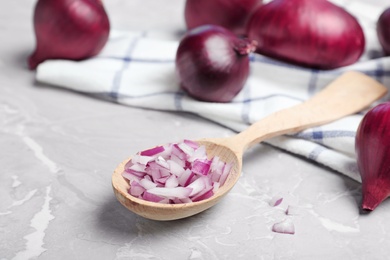 Photo of Spoon with cut and whole red onions and napkin on grey marble table