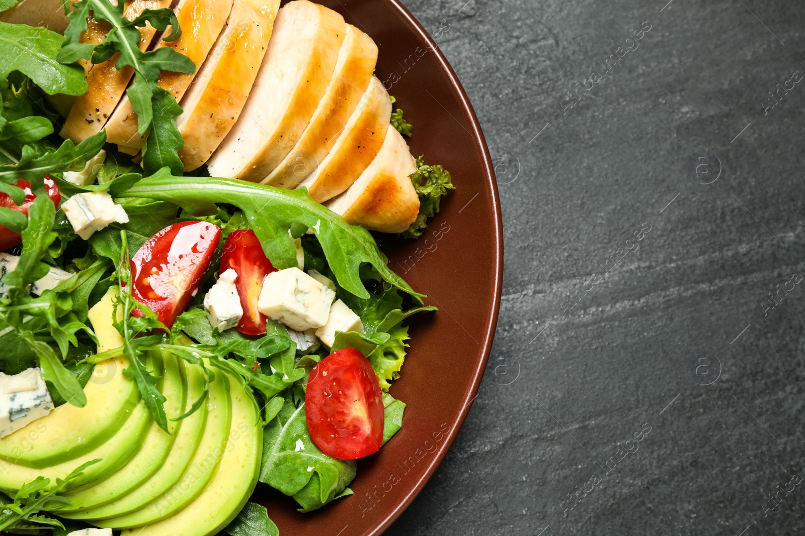 Photo of Delicious salad with chicken, arugula and avocado on black table, top view. Space or text