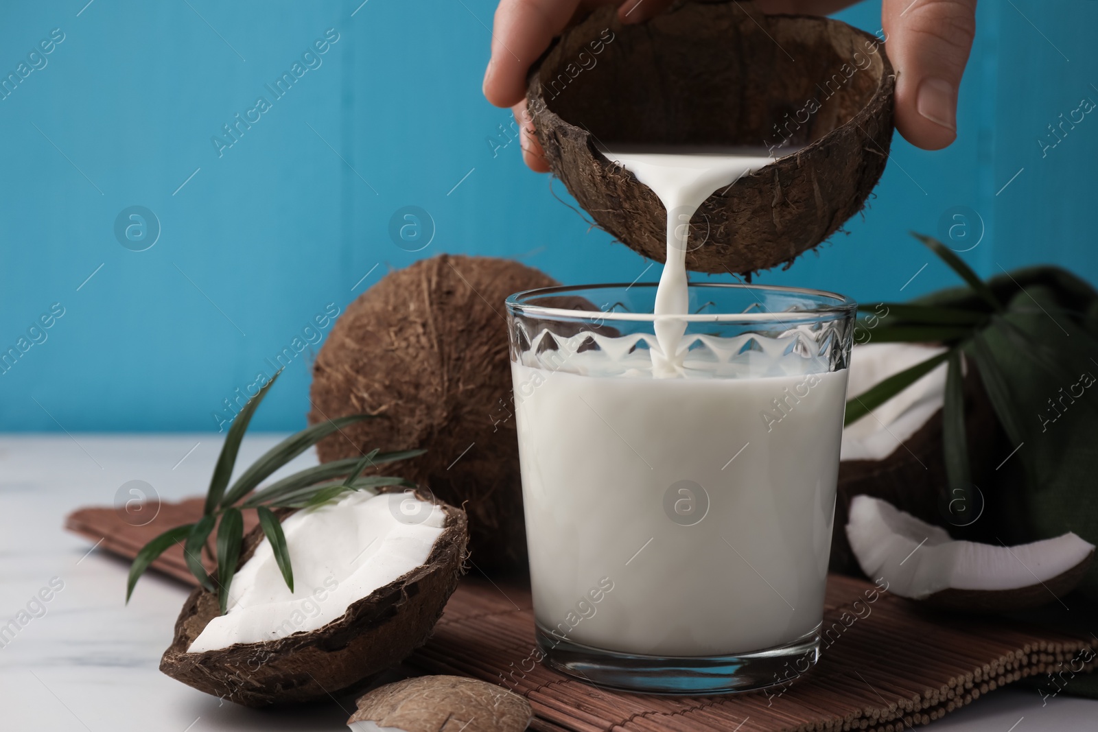 Photo of Woman pouring delicious coconut milk into glass at white marble table, closeup