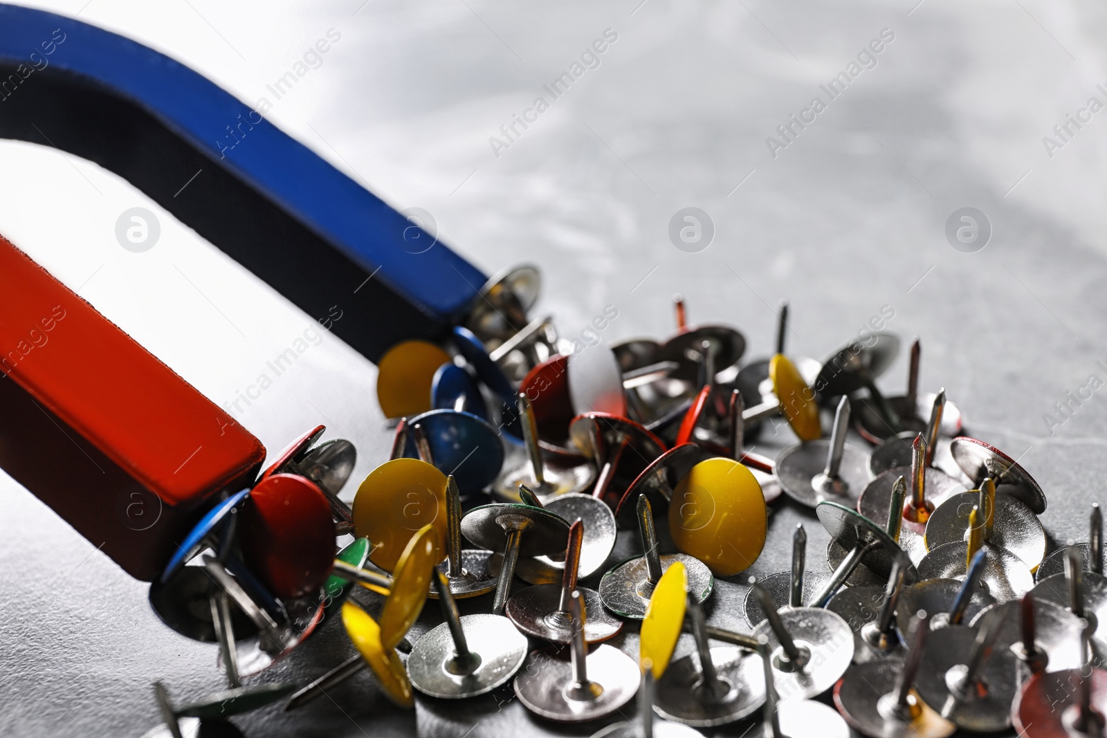 Photo of Red and blue horseshoe magnet attracting push pins over grey marble table, closeup