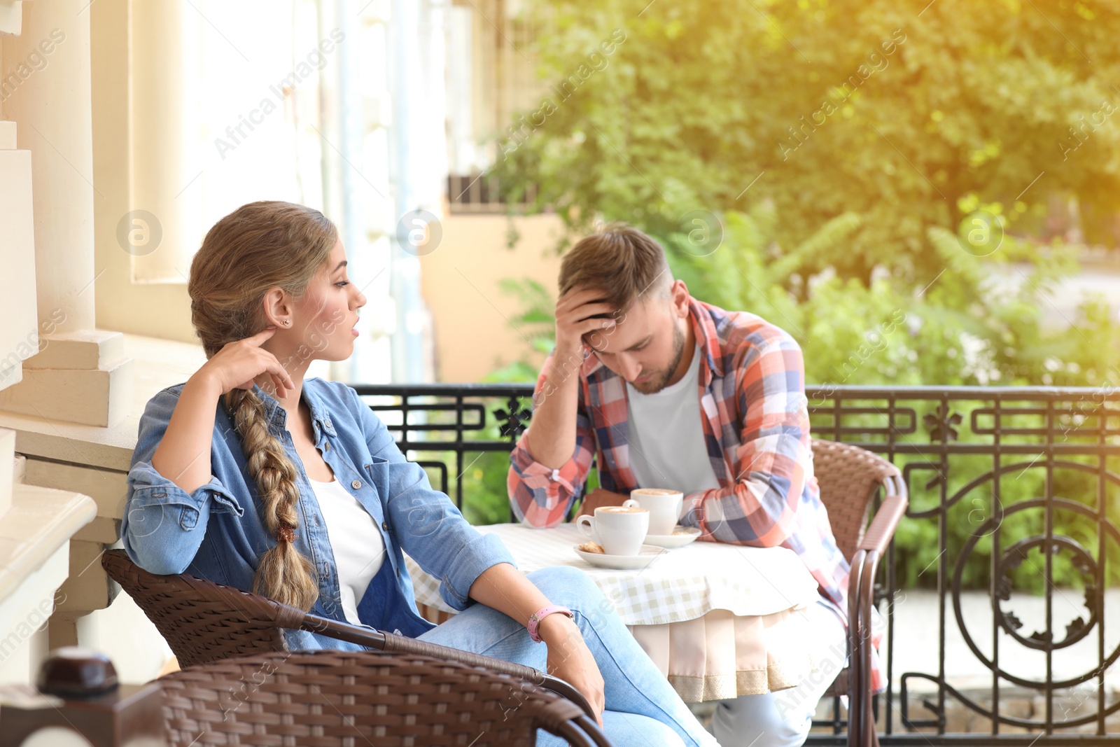 Photo of Young couple arguing while sitting in cafe, outdoors. Problems in relationship