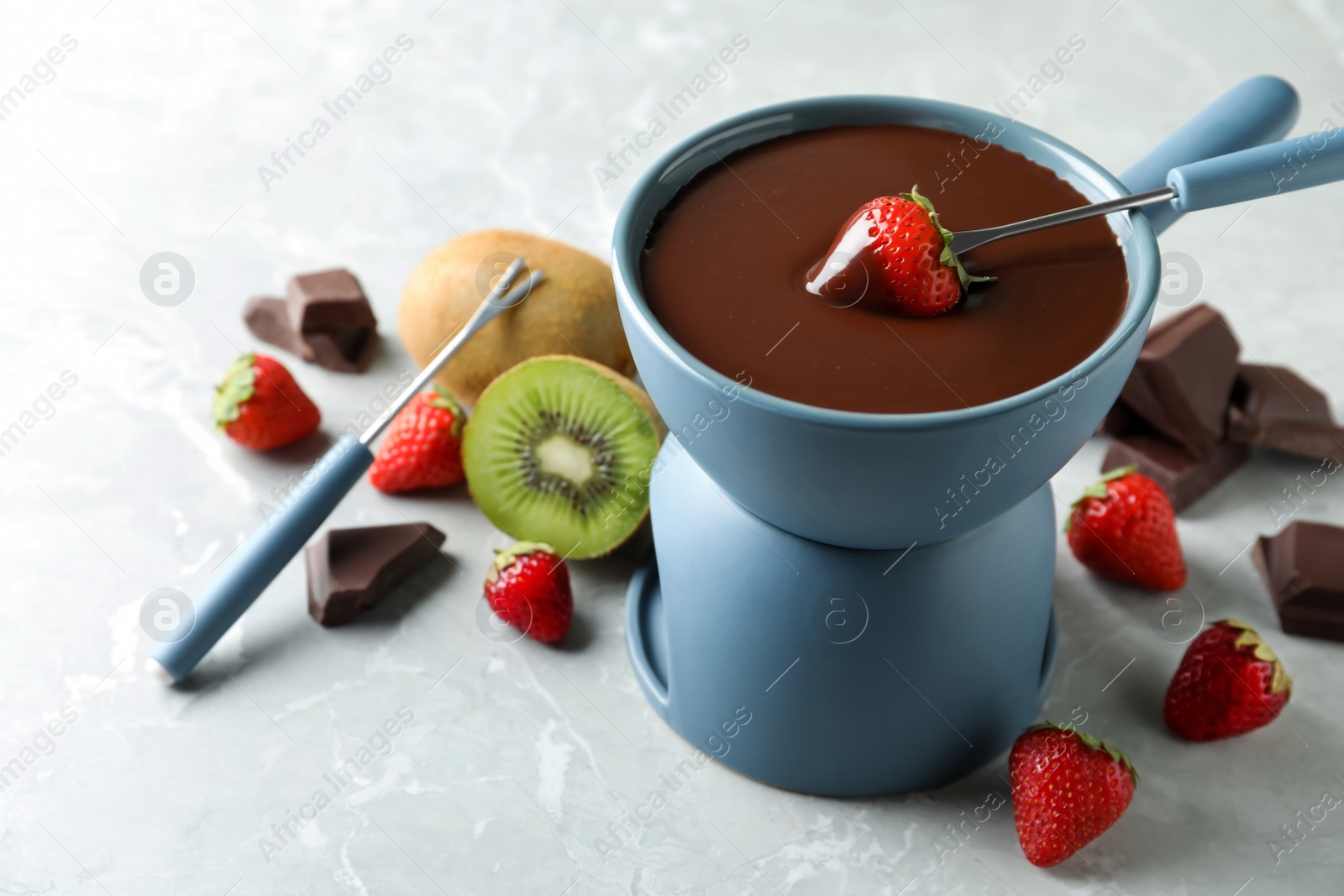 Photo of Dipping strawberry into fondue pot with chocolate on light marble table