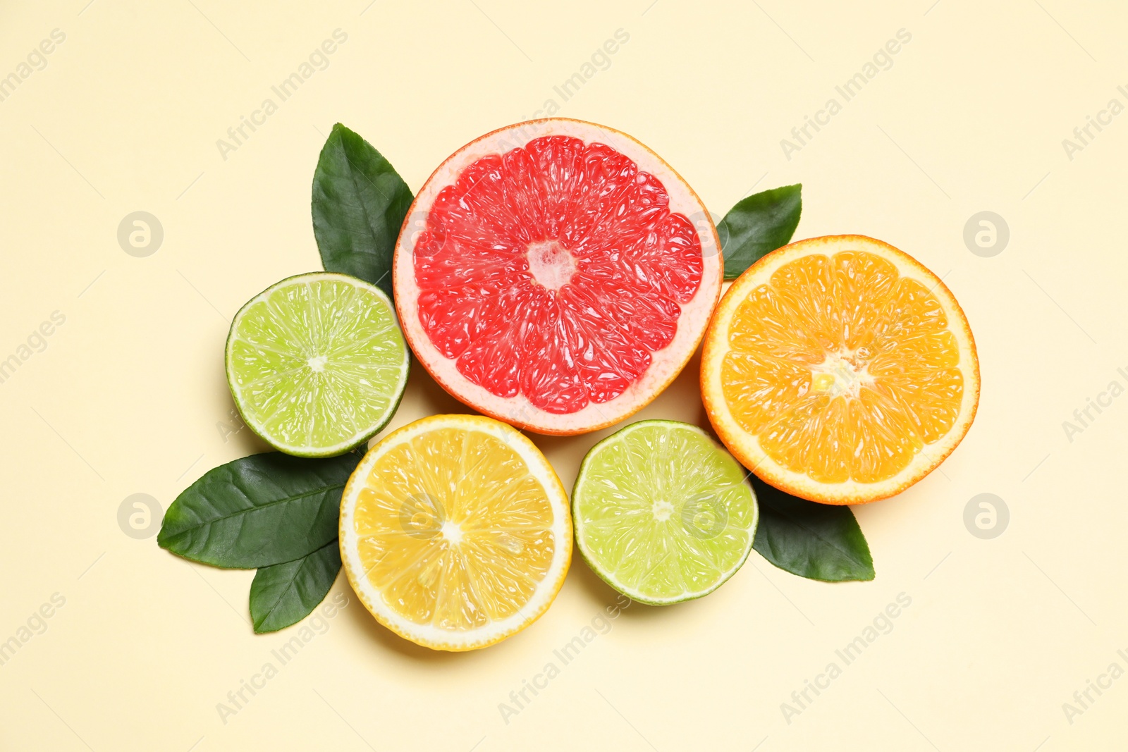 Photo of Different cut citrus fruits and leaves on beige table, flat lay