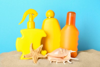 Different suntan products, seashell and starfish on sand against light blue background