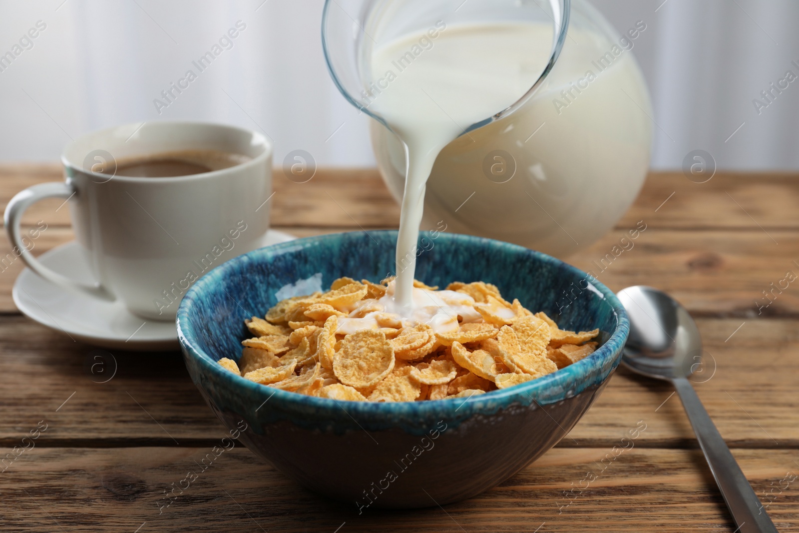 Photo of Pouring milk into bowl with healthy cornflakes on wooden table