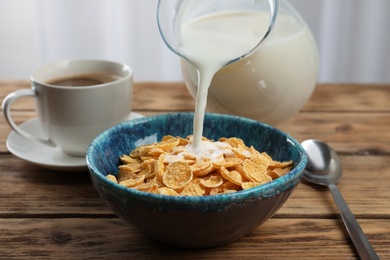 Photo of Pouring milk into bowl with healthy cornflakes on wooden table