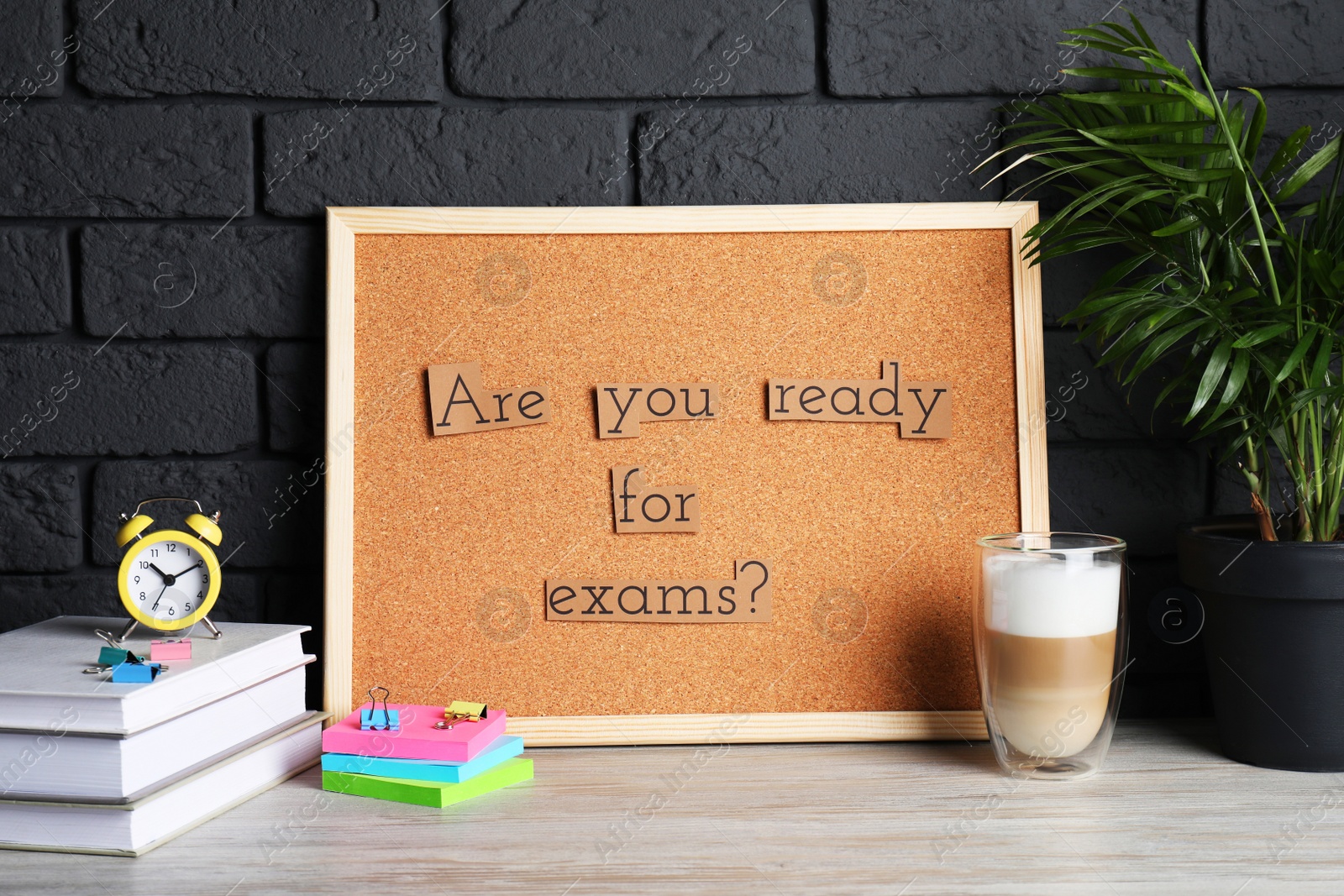 Photo of Cork board with phrase Are You Ready For Exams? on wooden table near black brick wall