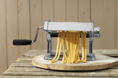 Pasta maker with raw dough on wooden table