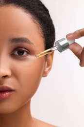 Woman applying serum onto her face on white background, closeup