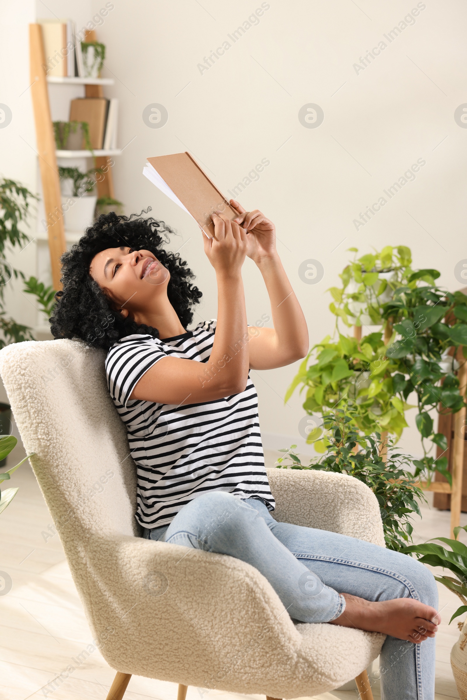 Photo of Relaxing atmosphere. Happy woman enjoying reading book near houseplants at home