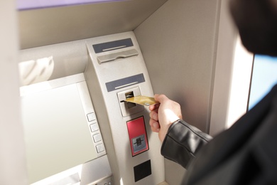 Man inserting credit card into cash machine outdoors, closeup