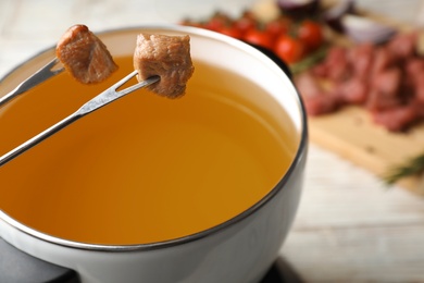 Photo of Dipping meat into fondue pot with oil on table, closeup