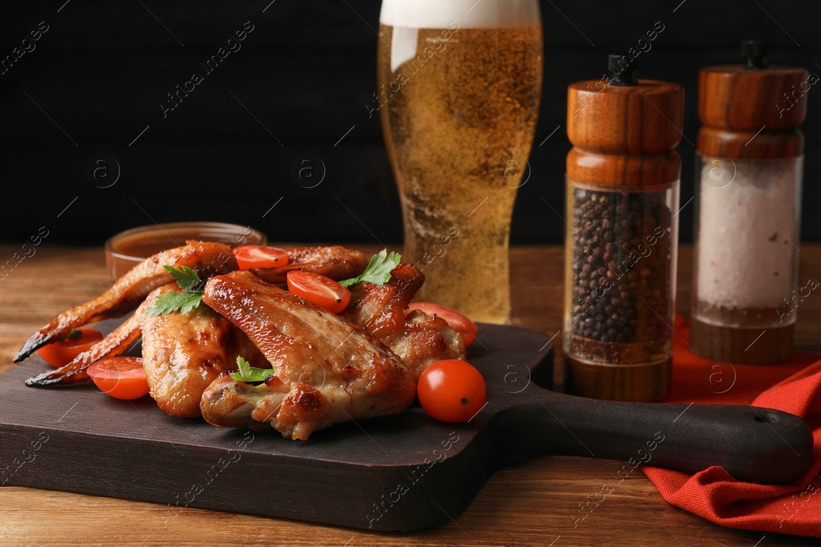 Photo of Glass of beer and delicious baked chicken wings with ingredients on wooden table