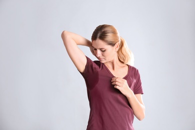 Young woman with sweat stain on her clothes against light background. Using deodorant