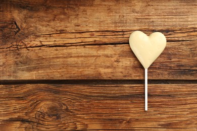 Photo of Chocolate heart shaped lollipop on wooden table, top view. Space for text