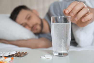 Photo of Man taking medicine for hangover in bed at home