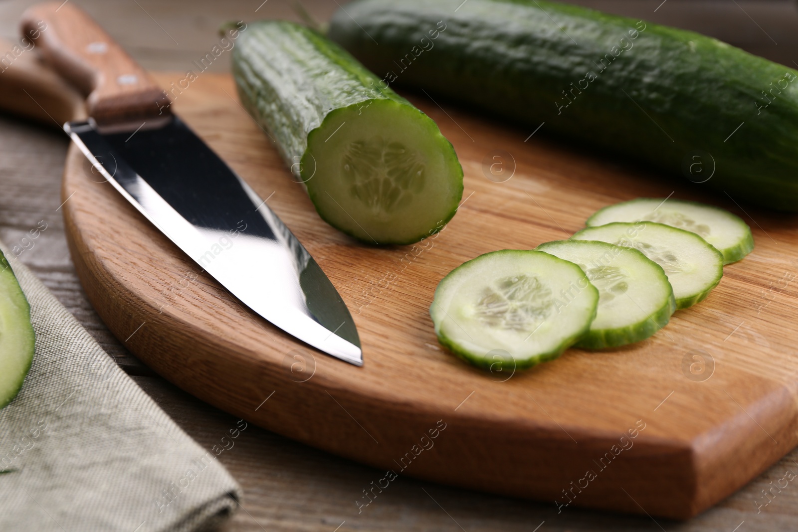 Photo of Sliced cucumber, knife and wooden cutting board on table, closeup