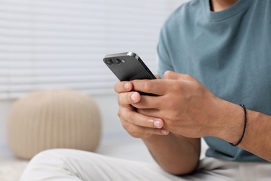 Man sending message via smartphone indoors, closeup