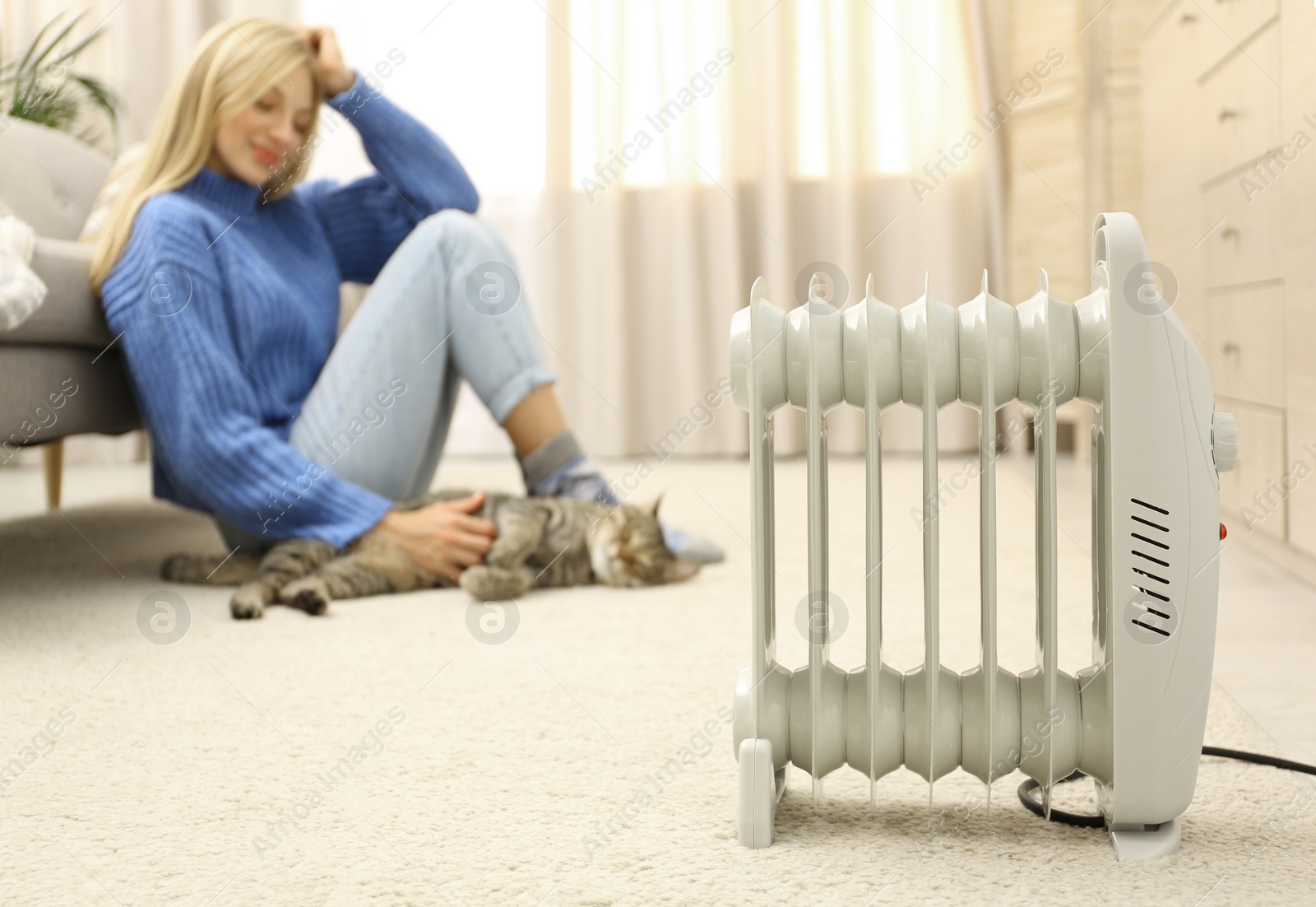 Photo of Electric heater and blurred young woman with cute tabby cat on background. Space for text