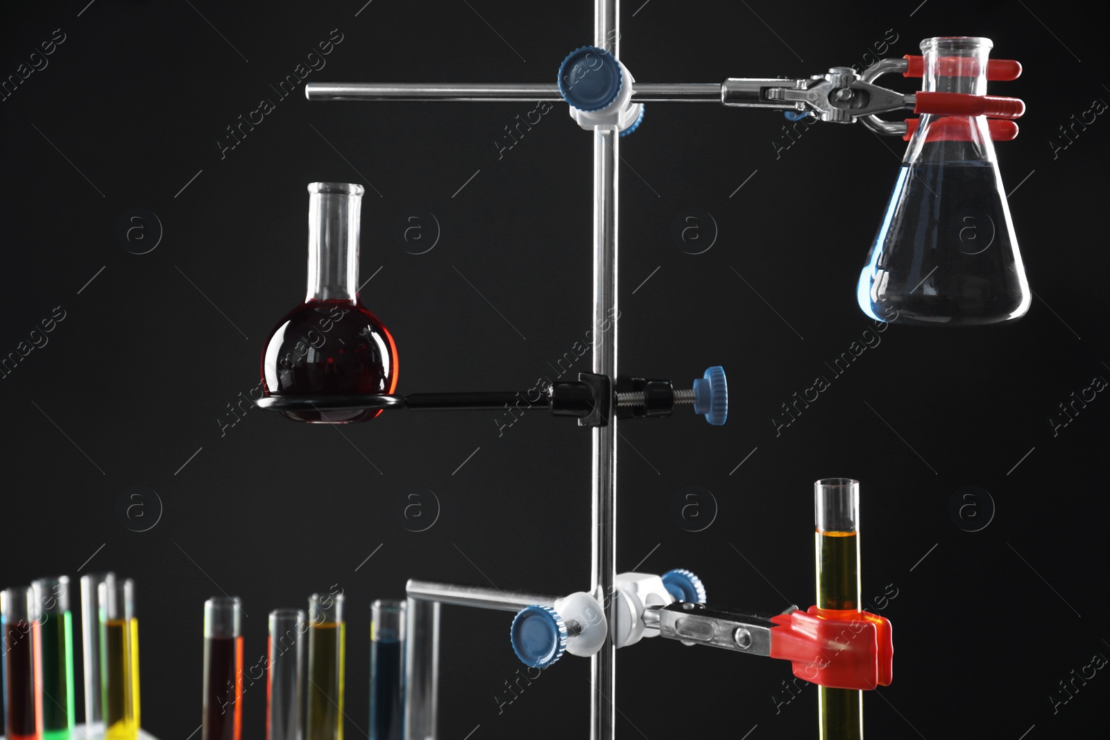 Photo of Retort stand and laboratory glassware with liquids on black background, closeup