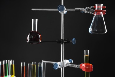 Retort stand and laboratory glassware with liquids on black background, closeup