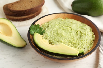 Photo of Bowl with guacamole made of ripe avocados served on white wooden table