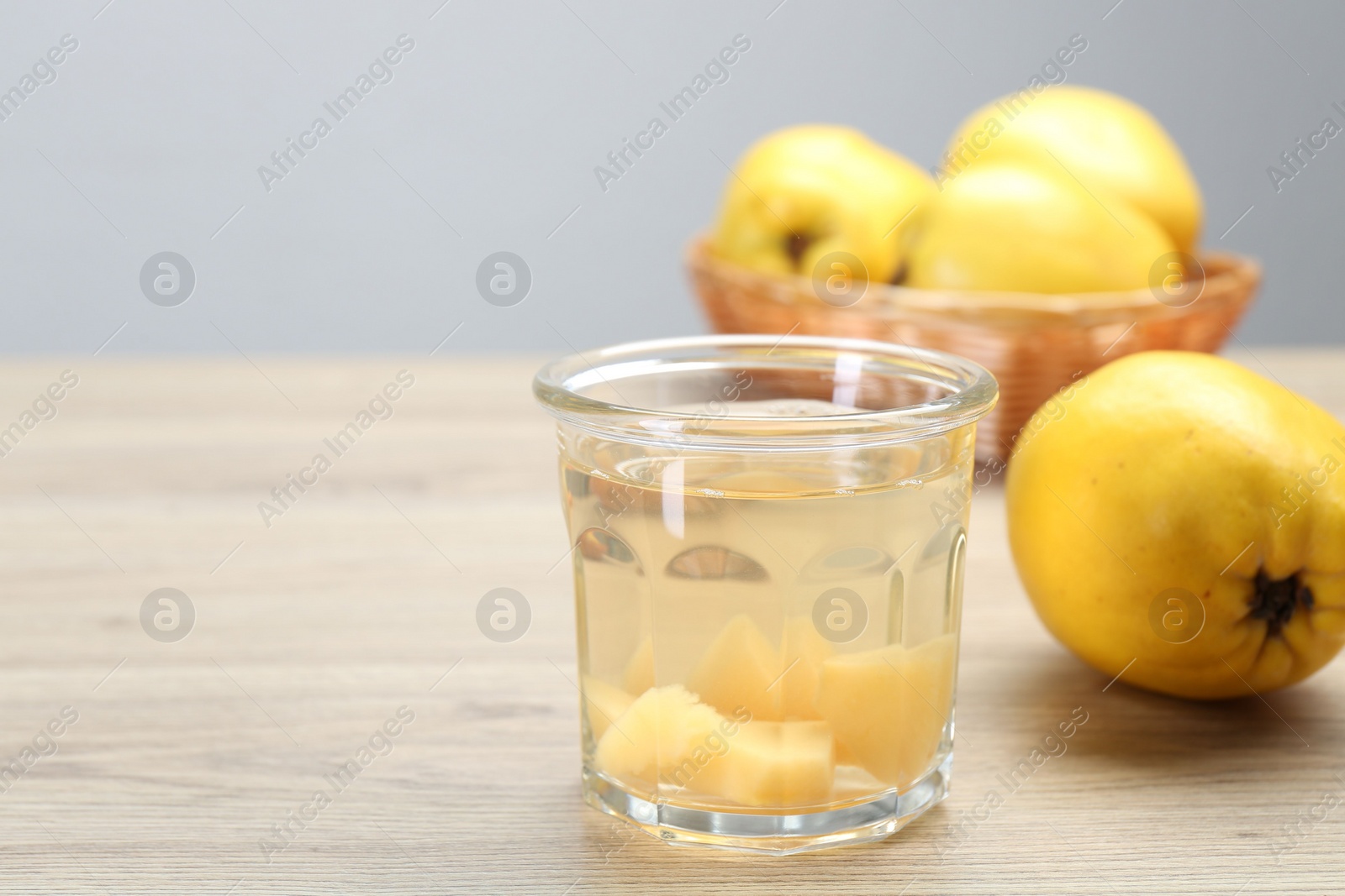 Photo of Delicious quince drink in glass and fresh fruits on wooden table, space for text